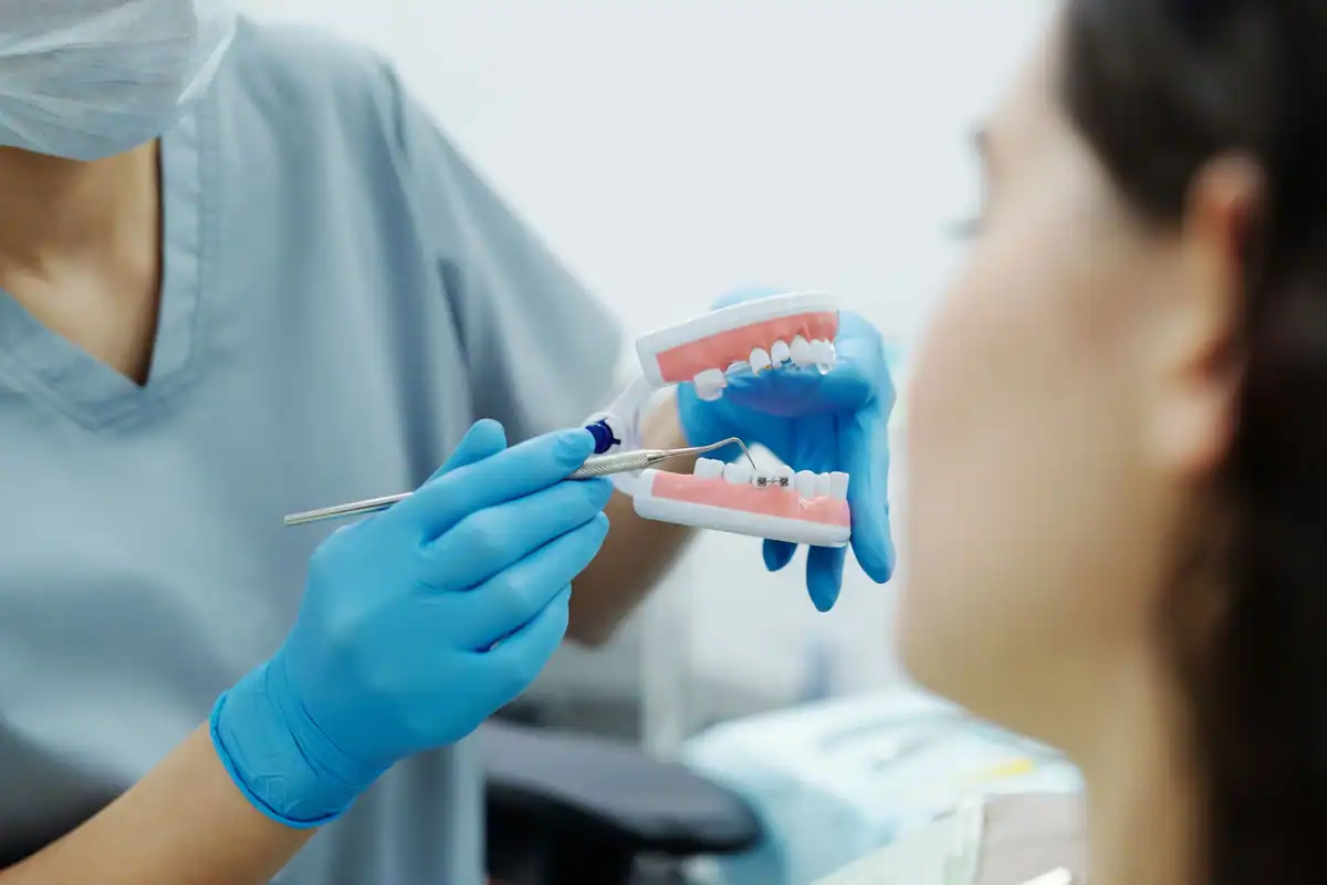Asistentă cu mănuși albastre arată pe un model dentar cum se curăță aparatul fix