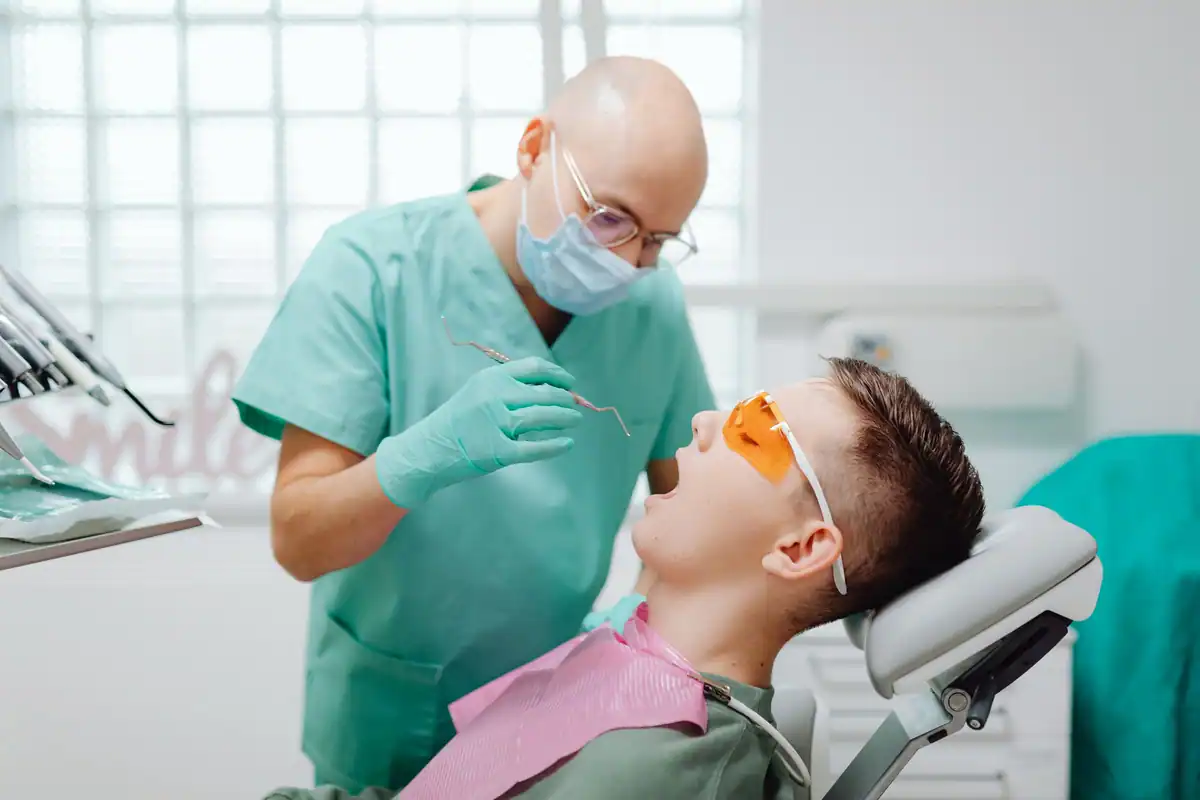 Medic în echipament verde examinează gingiile unui pacient aflat în fotoliul dentar