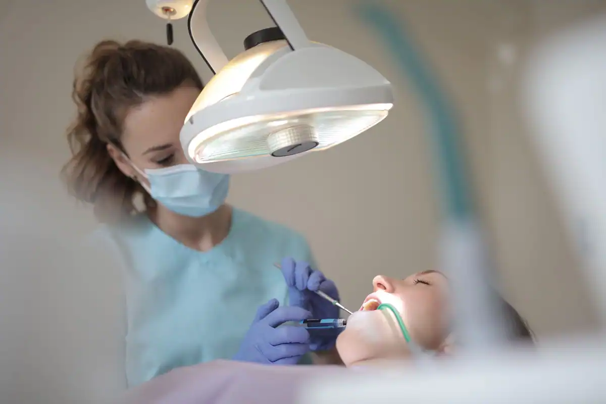 Medic stomatolog sub lampa chirurgicală lucrează la dinții unei paciente