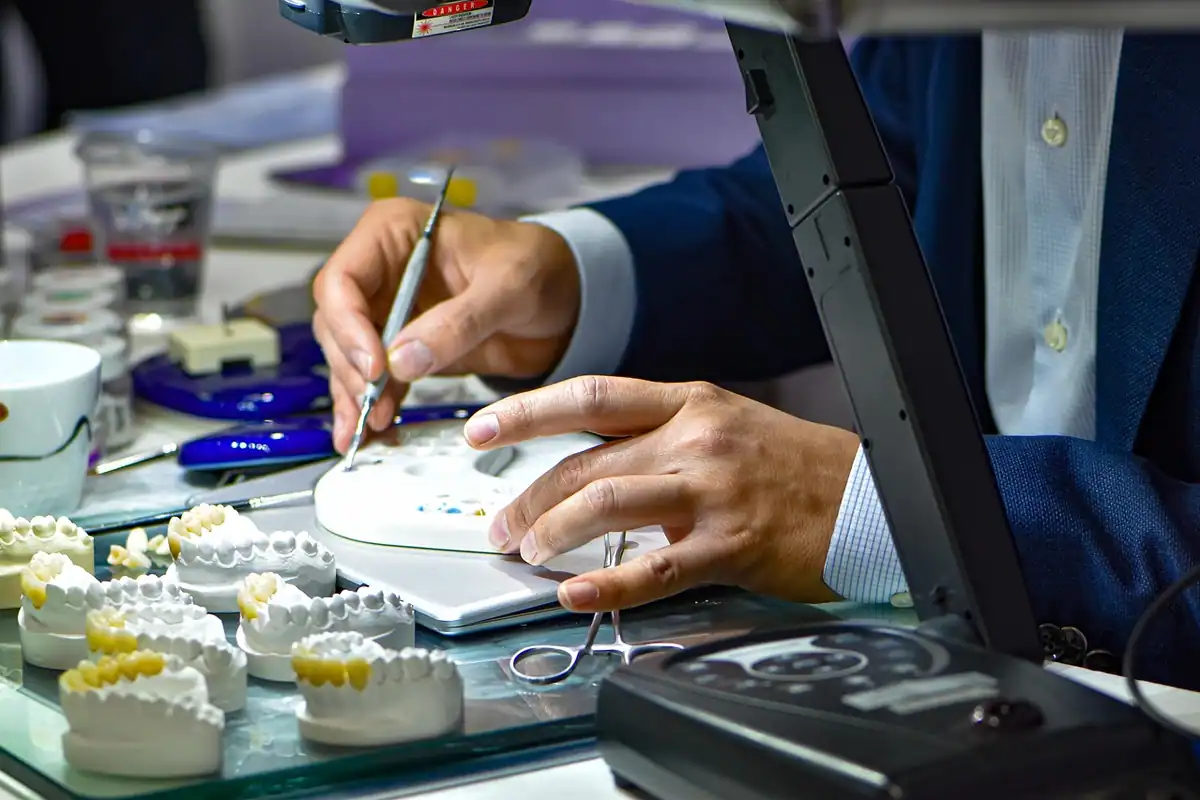Tehnician dentar modelează cu atenție o coroană pe modele din ghips la masa de lucru