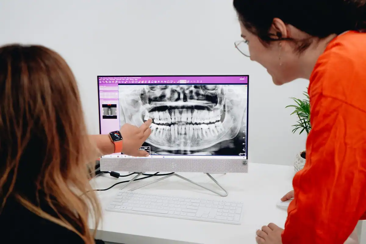 Două femei privesc o radiografie panoramică pe ecranul calculatorului dintr-o clinică dentară