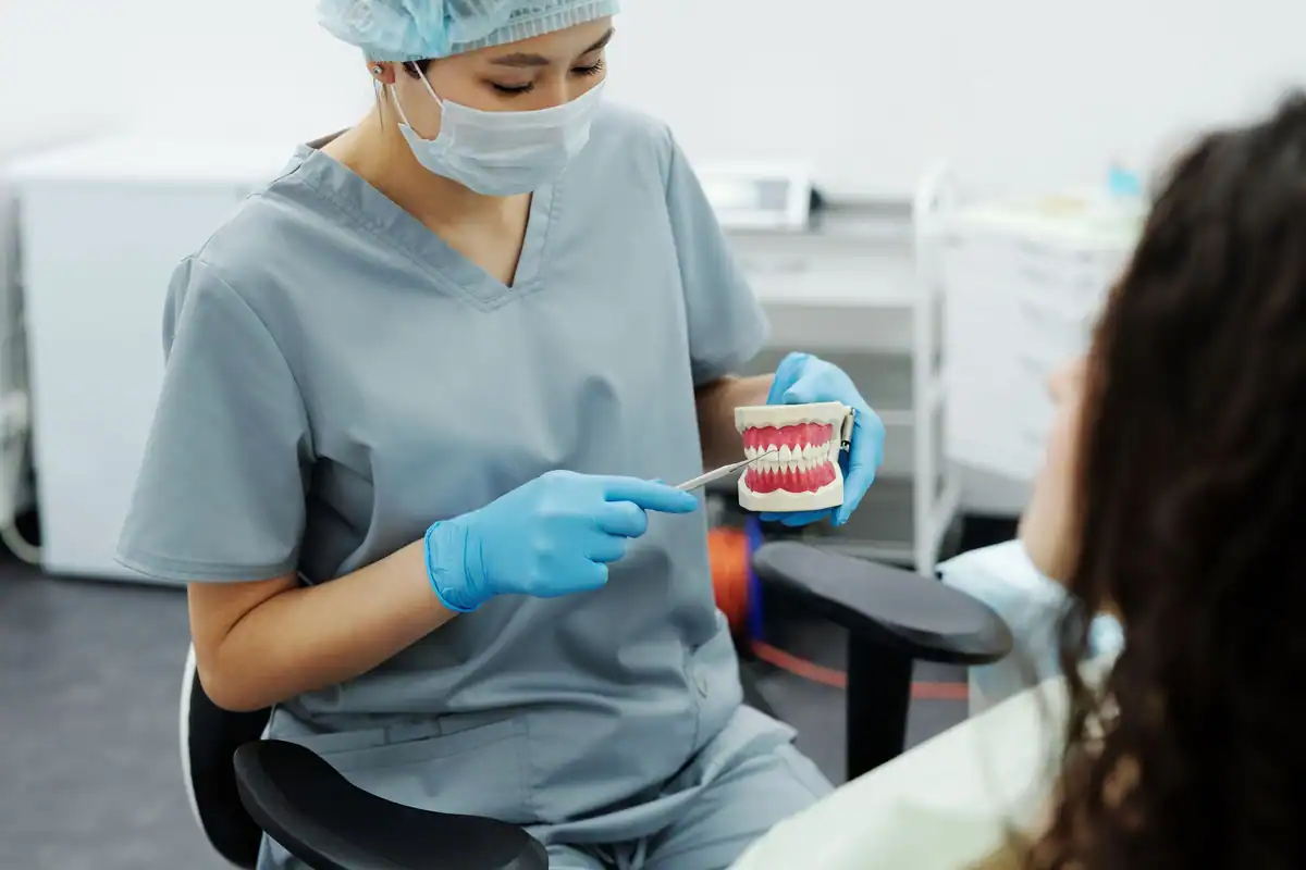 Asistentă într-un cabinet stomatologic explică pe un model dentar tratamentul ortodontic