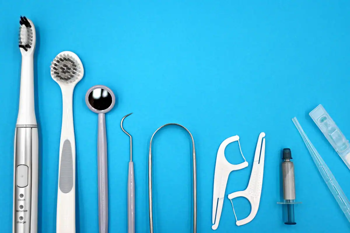 Periuțe, oglindă dentară, ață dentară și scobitori așezate pe un fundal albastru