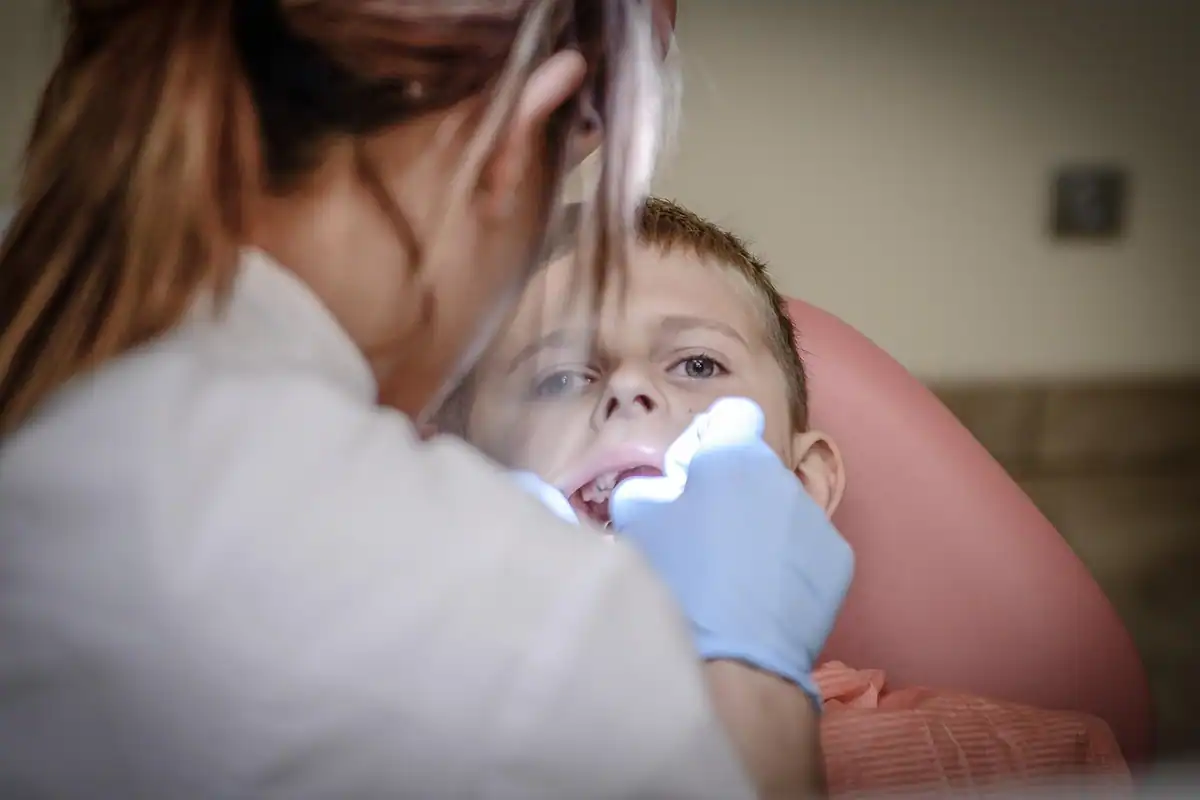 Medic cu mănuși tratează dinții unui copil așezat în fotoliul dentar
