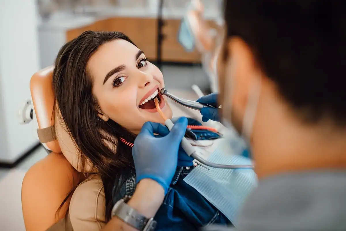 Pacientă zâmbitoare în fotoliul dentar, examinată de medic cu mănuși și mască