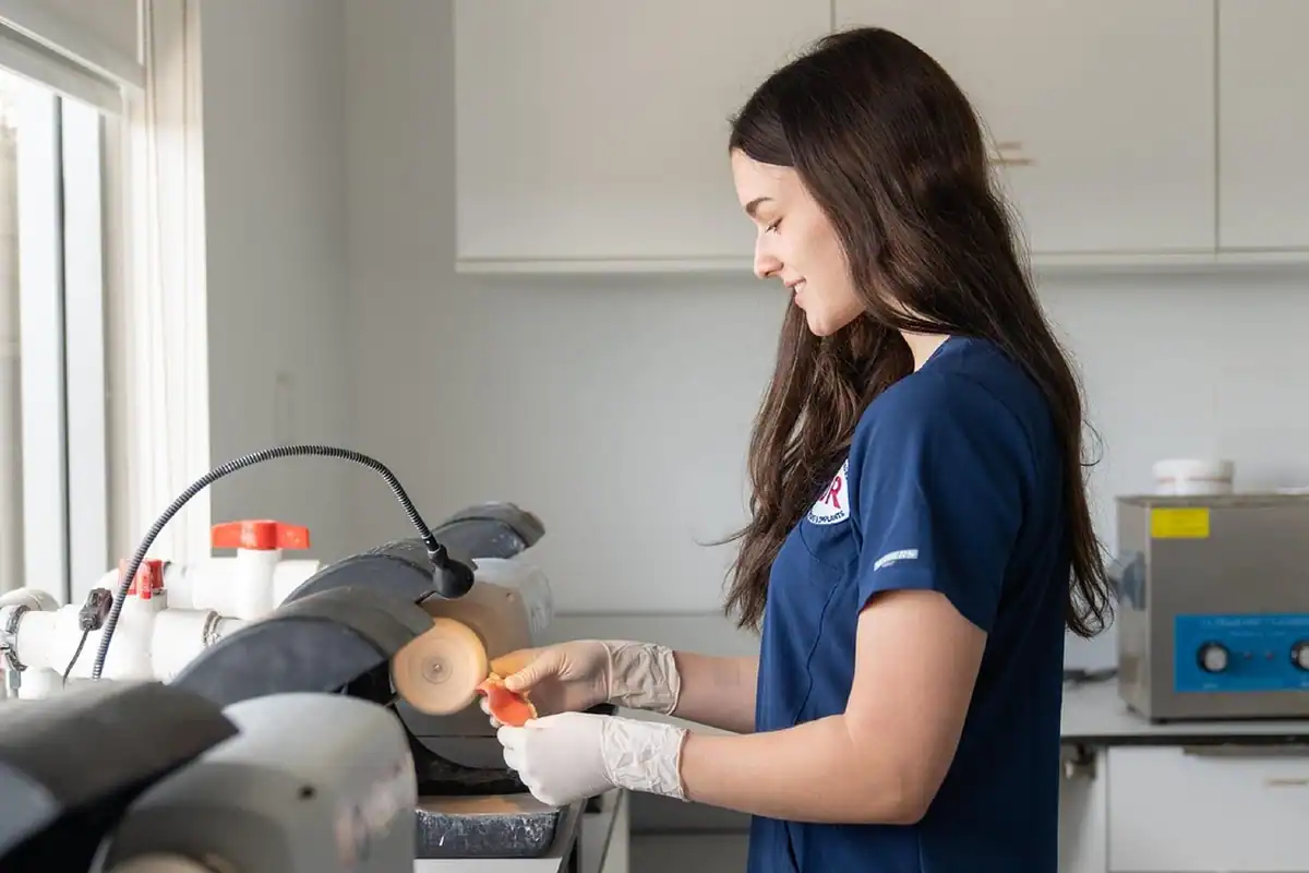 Tehnician în uniformă albastră lucrează la o proteză într-un laborator dentar