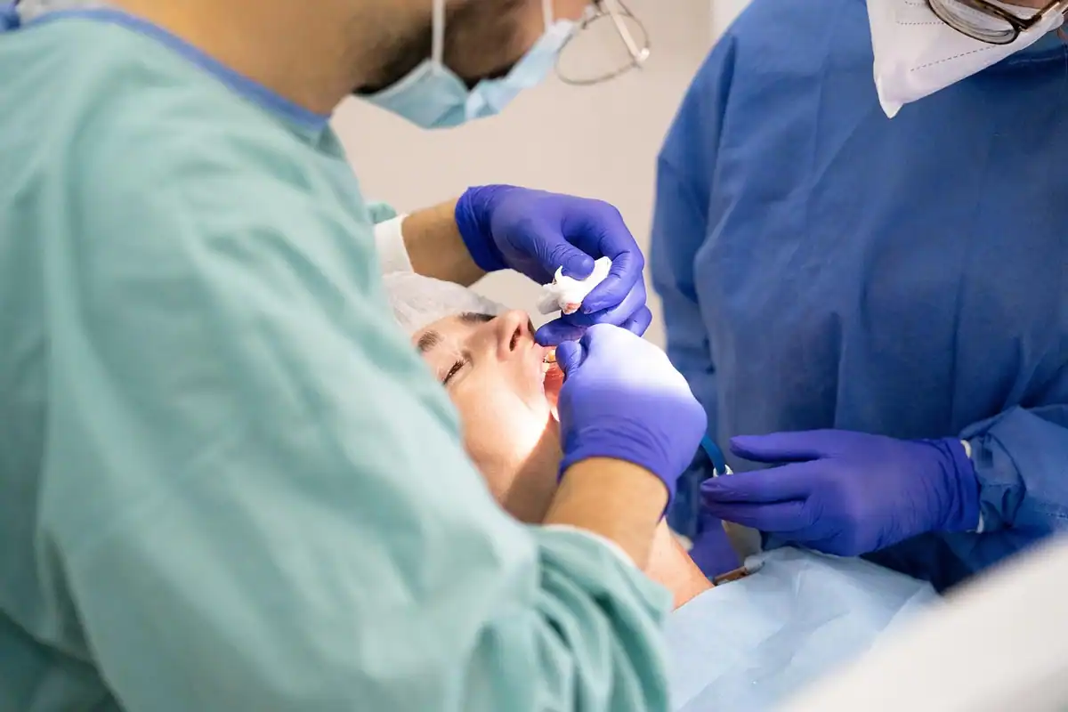 Doi medici cu mănuși albastre tratează un pacient întins în fotoliul dentar