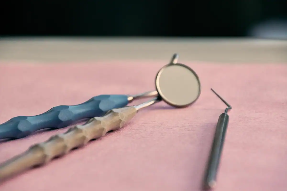 Oglindă și sondă dentară așezate pe un material roz, pregătite pentru consult